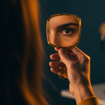 Primer plano cinematográfico del ojo de una mujer española reflejado en un espejo de mano ámbar, simbolizando el narcisismo.