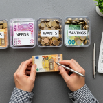 Manos organizando euros en tres frascos etiquetados '900€ Necesidades', '540€ Deseos', '360€ Ahorro'.