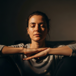 Primer plano cinematográfico de mujer española meditando serenamente con luz suave, manos en el regazo, expresión de paz.