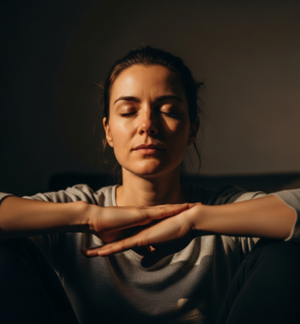 Primer plano cinematográfico de mujer española meditando serenamente con luz suave, manos en el regazo, expresión de paz.
