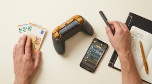 Vista cenital de un controlador de juego, billetes de euro, un cuaderno con 'Ingresos GTA VI' y un smartphone con interfaz de juego.