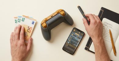 Vista cenital de un controlador de juego, billetes de euro, un cuaderno con 'Ingresos GTA VI' y un smartphone con interfaz de juego.