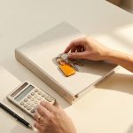 Llaves de casa y documento de seguro de hogar sobre mesa crema con calculadora