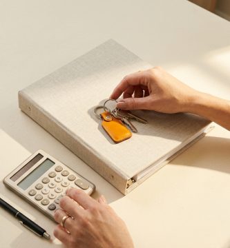 Llaves de casa y documento de seguro de hogar sobre mesa crema con calculadora