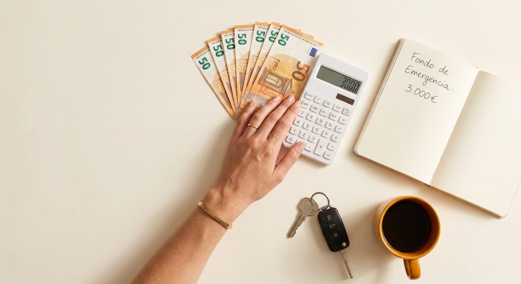 Fondo de emergencia en euros con libreta de notas, calculadora y llaves sobre fondo crema